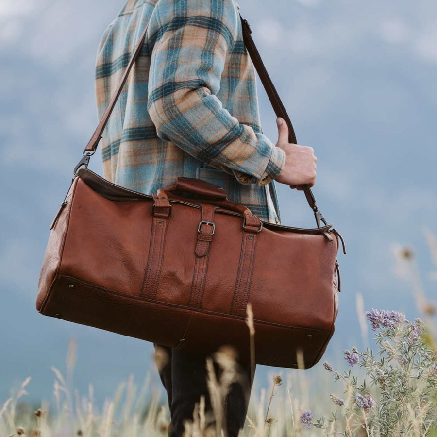 A brown full-grain leather duffle bag with a structured design and visible stitching details.